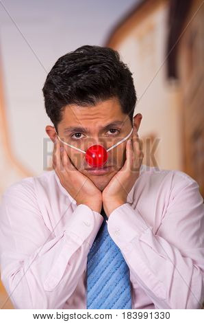 Unhappy handsome businessman with red plastic nose.