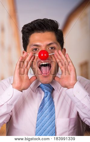 Funny handsome businessman with red plastic nose screaming.