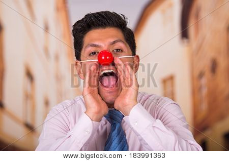Funny handsome businessman with red plastic nose screaming.