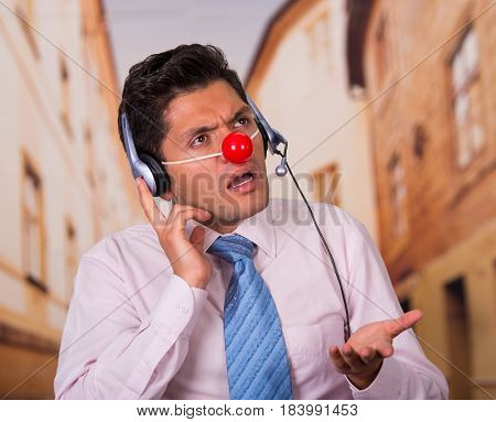 Funny handsome businessman with red plastic nose using headphones. and he is looks surprised.
