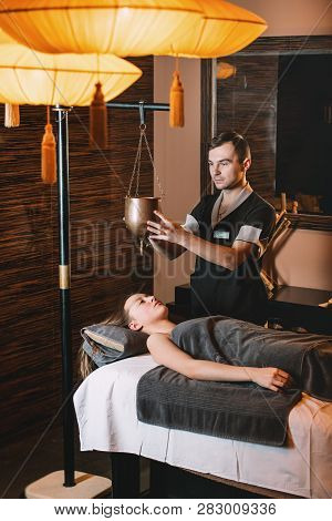 Specialist Making Shirodhara Massage Form Of Ayurveda Therapy. Beautiful Woman Spending Time At Mode