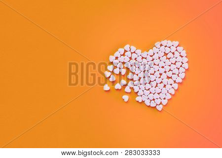 White Heart Shaped Candies On An Orange Paper Background. Broken Heart Or Pearts Gethering Love Conc