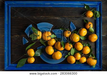 Сomposition From Fresh Mandarins With Broken Plate In A Blue Frame On A Wood Background. Creative Co
