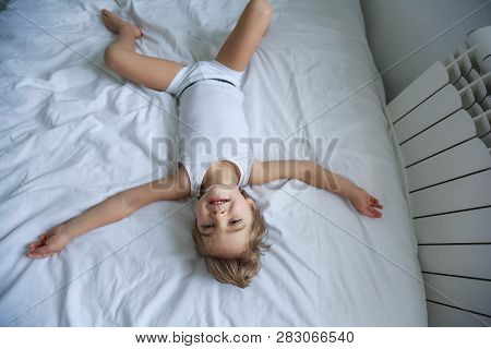 Happy Boy Playing In White Bedroom. Little Boy Brother Play On The Bed Wearing Pajamas. Family At Ho