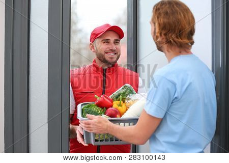 Courier Giving Plastic Crate With Products To Customer At Home. Food Delivery Service