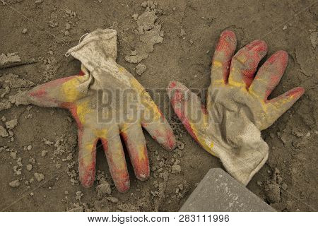 A Pair Of Working Gloves With Yellow And Red Fingers Lying On The Wet Sand And A Piece Of Gray Pavin