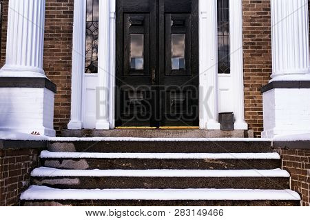 The Snow Covered Steps To An Old Brick House With White Pillars In Torrington, Connecticut.