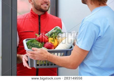 Courier Giving Plastic Crate With Products To Customer At Home, Closeup. Food Delivery Service