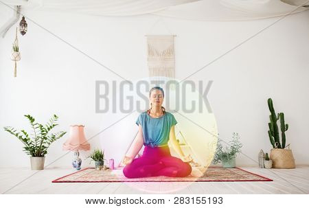 mindfulness, spirituality and healthy lifestyle concept - woman meditating in lotus pose at yoga studio over rainbow aura circle