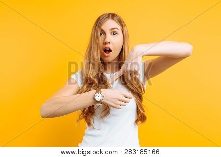 Beautiful Girl Looking At A Hand Watch, Points To The Watch, On A Yellow Background, Concept Of Bein