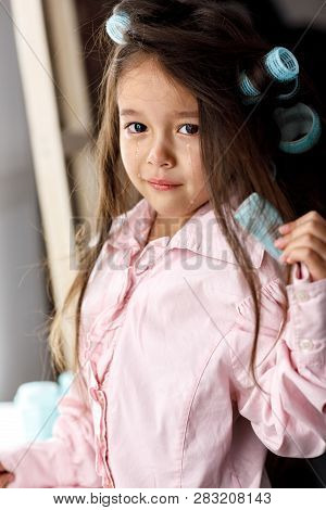 Crying Little Girl Tries To Remove The Hair Curlers Herself In Front Of The Mirror At Home