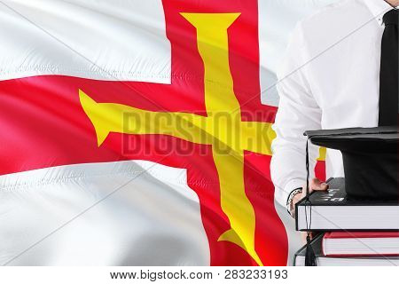 Successful Student Education Concept. Holding Books And Graduation Cap Over Guernsey Flag Background