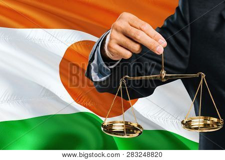 Nigerien Judge Is Holding Golden Scales Of Justice With Niger Waving Flag Background. Equality Theme