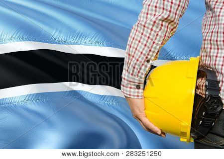Engineer Is Holding Yellow Safety Helmet With Waving Botswana Flag Background. Construction And Buil