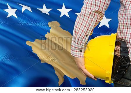 Engineer Is Holding Yellow Safety Helmet With Waving Kosovo Flag Background. Construction And Buildi