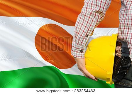 Nigerien Engineer Is Holding Yellow Safety Helmet With Waving Niger Flag Background. Construction An