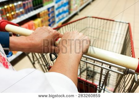 Person Pushing Shopping Trolley Cart Against Modern Supermarket Aisle Background