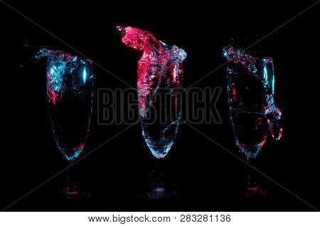 Beverage Splashing Into Three Separate Champagne Flutes Under Red And Blue Lights On A Black Backgro