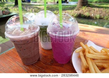 Three Glasses Of Soft Drink, Iced Chocolate And Milk Green Tea With French Fries On Wooden Square Ta