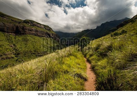 The Tugela Gorge Hiking Trail Leading Along A Brightly Lit Hillside Towards The Amphitheatre Mountai