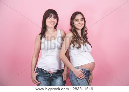 Maternity Concept, Two Beautiful Pregnant Women With An Open Tummy In Jindes And White T-shirts On A