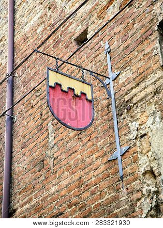 Metallic Plaque Of A Medieval Embattled Shield On A Brick Facade Of Asti, Piedmont, Italy.