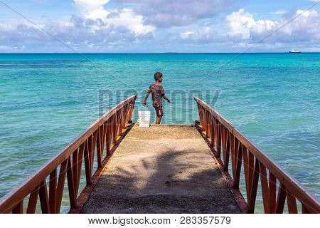 A Local Polynesian Boy Fishing From A Jetty Pier In A Tropical Azure Turquoise Blue Lagoon At Vaiaku