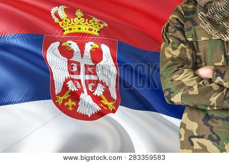 Crossed Arms Serbian Soldier With National Waving Flag On Background - Serbia Military Theme.