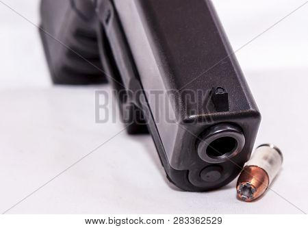 A Black 9mm Pistol Shown With A Single 9mm Bullet On A White Background