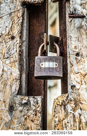 Abandoned Building, With A Fiberboard Gate Closed With A Padlock In The Foreground - Focus On The Pa