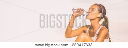 True wireless earbuds fitness woman drinking water bottle during fit workout outdoor on panoramic white background. Happy asian girl healthy lifestyle banner panorama.