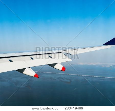 Aircraft Wing With Red Tipped Pillion In Flight  Above Ocean Coastline With City Buildings And Bridg