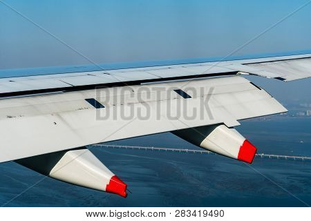 Aircraft Wing With Red Tipped Pillion In Flight  Above Ocean Coastline With City Buildings And Bridg