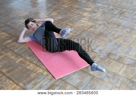 A Girl In A Gray T-shirt On A Pink Rug Alternately Raises Her Legs To Her Chest. Fitness Exercise To