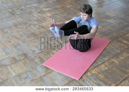 A Girl In A Gray T-shirt On A Pink Rug Raises Her Legs. Fitness Exercise To Strengthen The Abdominal
