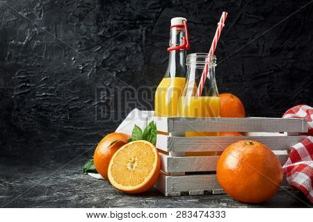 Freshly squeezed orange juice in glass bottle with straw white wooden box Fruity still life on black backdrop and grey concrete surface rustic style.