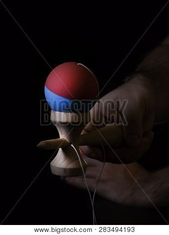 Classic Japanese Game Kendama On Black Background. Two Boys Hands Playing Kendama