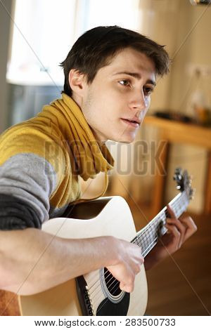 A Guy In A Yellow Sweater Sings A Song, Playing At His Guitar At Home On A Sunny Day