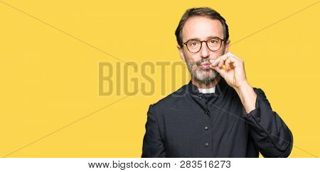 Middle age priest man wearing catholic robe mouth and lips shut as zip with fingers. Secret and silent, taboo talking