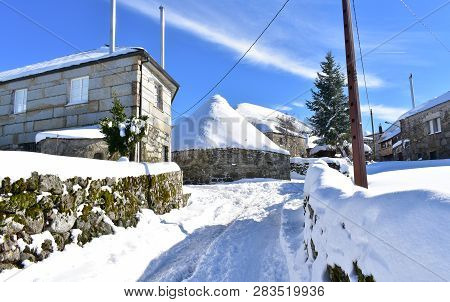 Piornedo, Ancares, Lugo Province, Galicia, Spain. Ancient palloza houses made with stone and straw with spruce. Snowy mountain village, blue sky, sunny day.