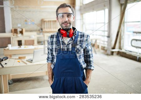 Happy Confident Middle-aged Bearded Joiner In Protective Goggles Wearing Ear Protectors On Neck Stan