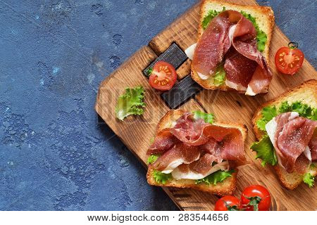 Bruschetta With Prosciutto, Salad Frieze And Cheese On The Kitchen Table. Snack. View From Above.