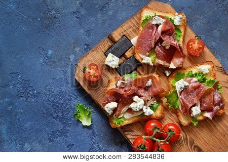 Bruschetta With Prosciutto, Salad Frieze And Cheese On The Kitchen Table. Snack. View From Above.