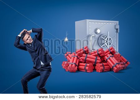 Businessman Covering His Head To Protect Himself From An Upcoming Blow Of Big Heap Of Dynamite Besid