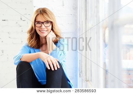 Happy Mature Woman Looking At Camera And Smiling While Relaxing At The Window