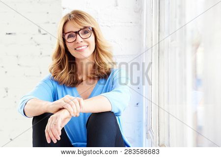 Happy Mature Woman Looking At Camera And Smiling While Relaxing At The Window