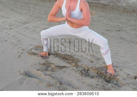 Young Woman Doing Yoga Plie Squat On The Sandy Beach At Sunrise.