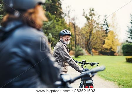 Active Senior Couple With Electrobikes Standing Outdoors On A Road In Nature.