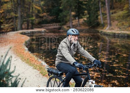 A Senior Man With Electrobike Cycling Outdoors On A Road In Park In Autumn.