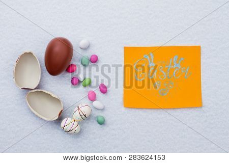 Broken Chocolate Egg On Light Background. Styrofoam Easter Eggs And Colorful Candies. Easter Greetin